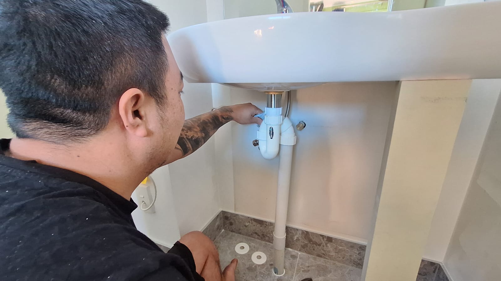 TradePlus handyman tightening the waste trap under a bathroom basin in an Auckland home