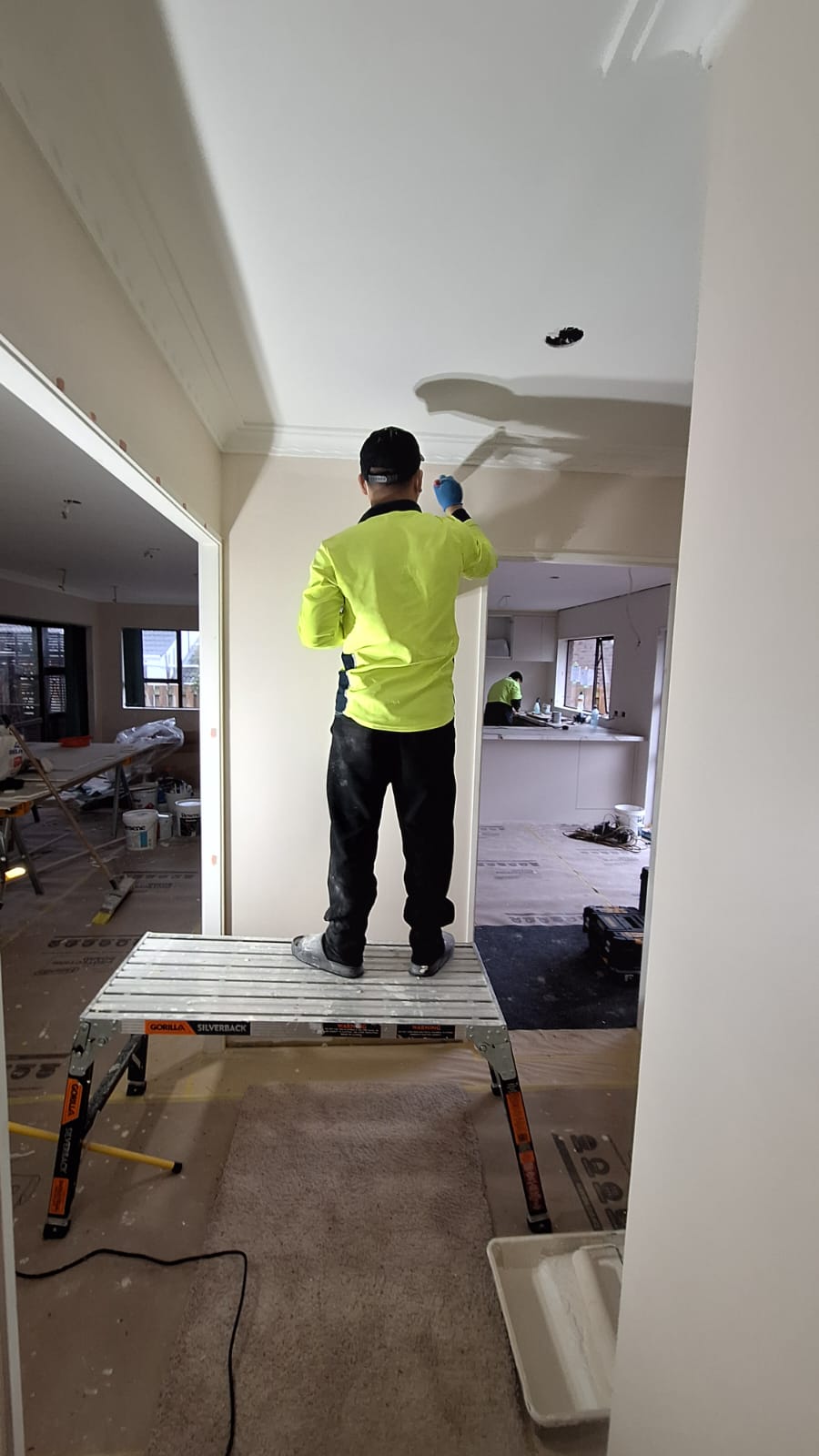TradePlus handyman on a work platform patching and painting an interior ceiling in an Auckland home